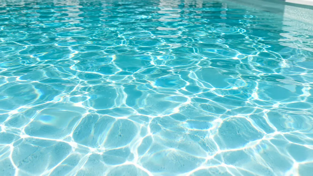 Close-up of crystal clear pool water with sunlight ripple patterns across a white plaster floor.